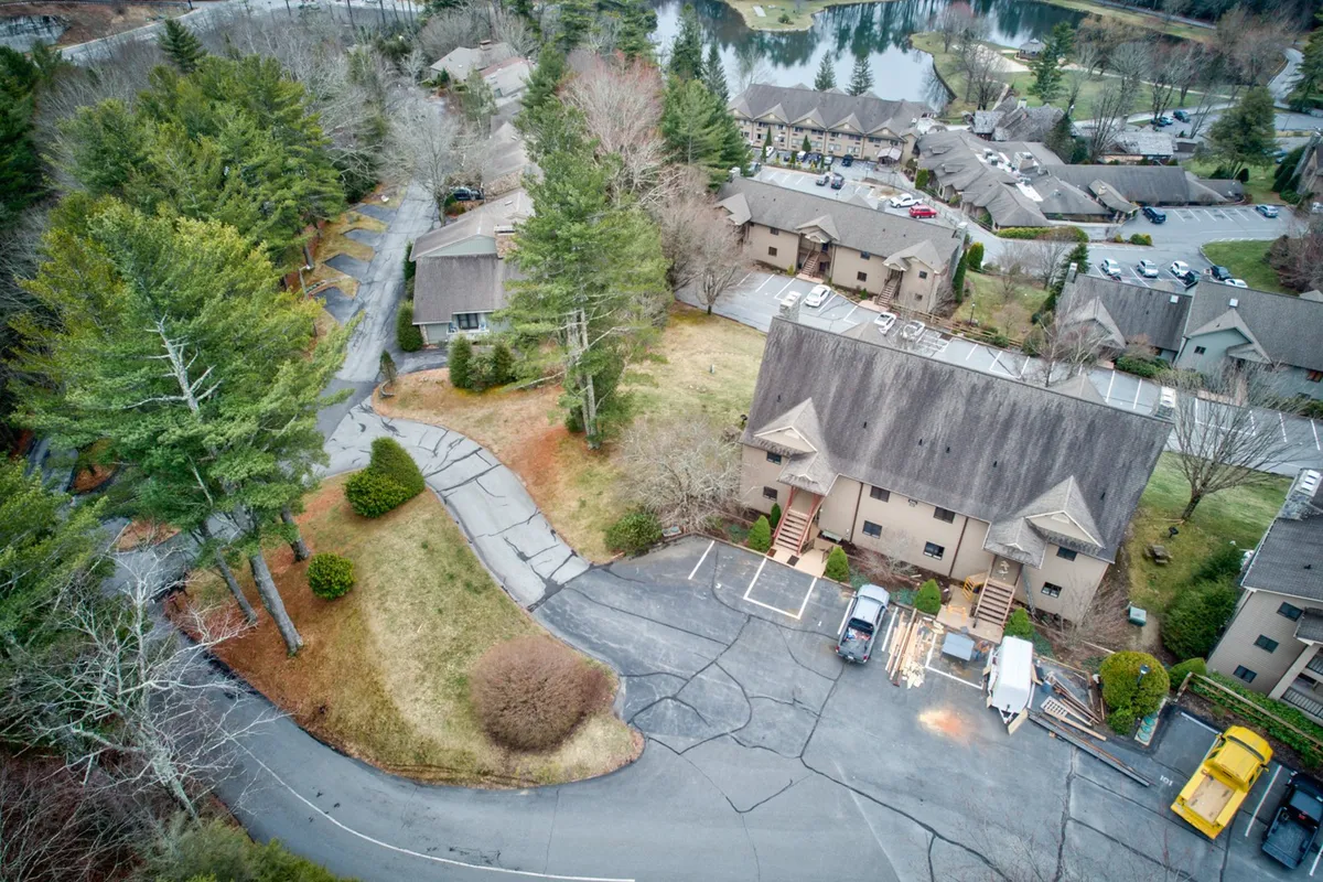 The photo features the resort’s exterior buildings nestled among trees, with a peaceful lake visible nearby. The landscape encourages exploration of resort amenities, highlighting access to both natural beauty and recreational facilities.