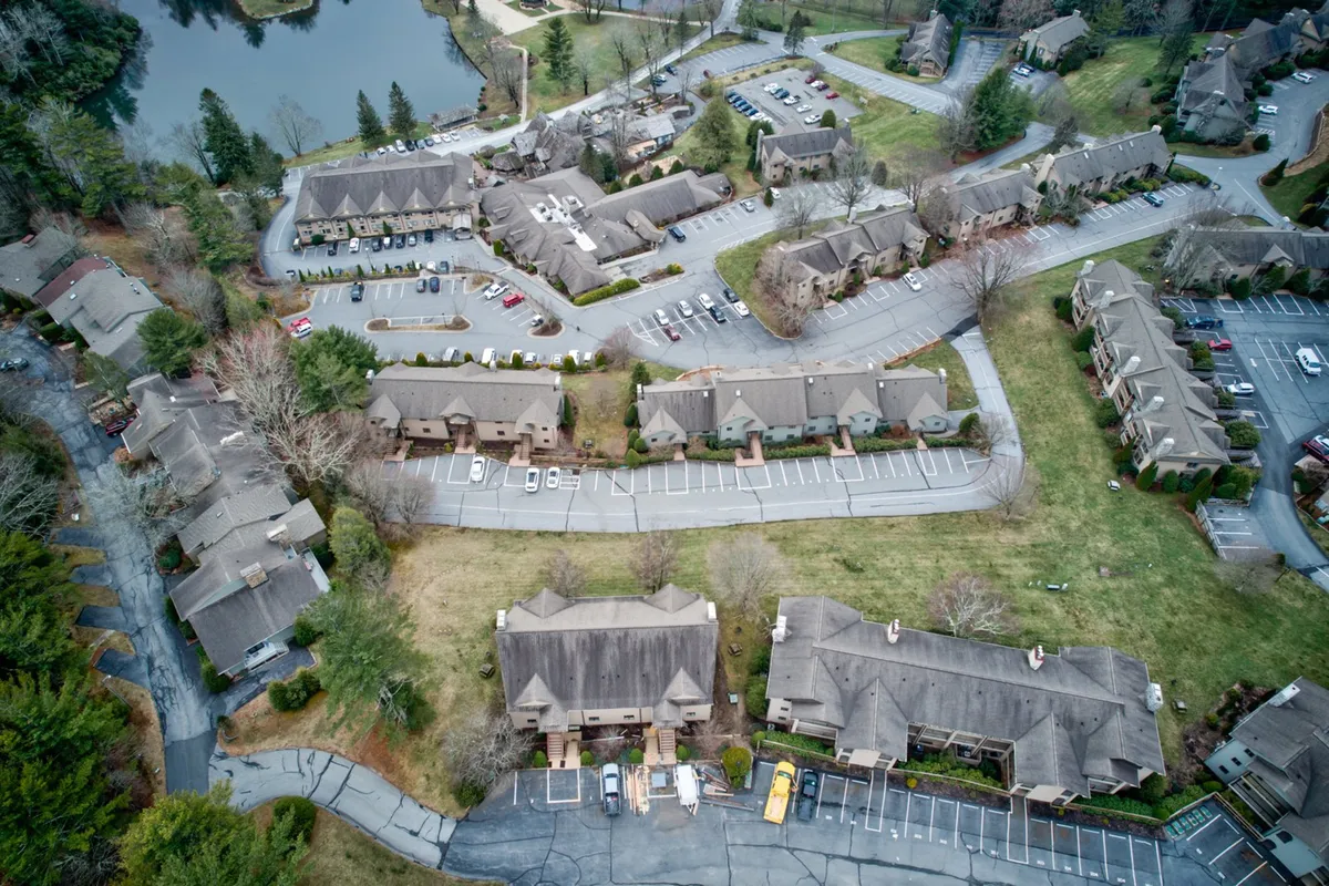 An aerial perspective showcases resort buildings nestled beside a scenic lake, surrounded by parking areas, green lawns, and walking paths. The image hints at communal spaces and the broader resort environment ideal for family strolls, fishing, and outdoor play.