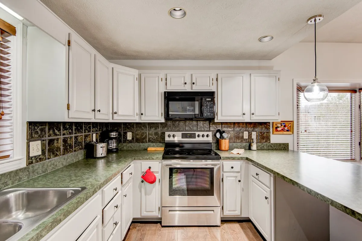 A newly updated kitchen featuring a sleek stainless steel stove, green countertops, white cabinetry, and modern kitchen accessories. The space is designed for both culinary creativity and convenient family meal preparation.