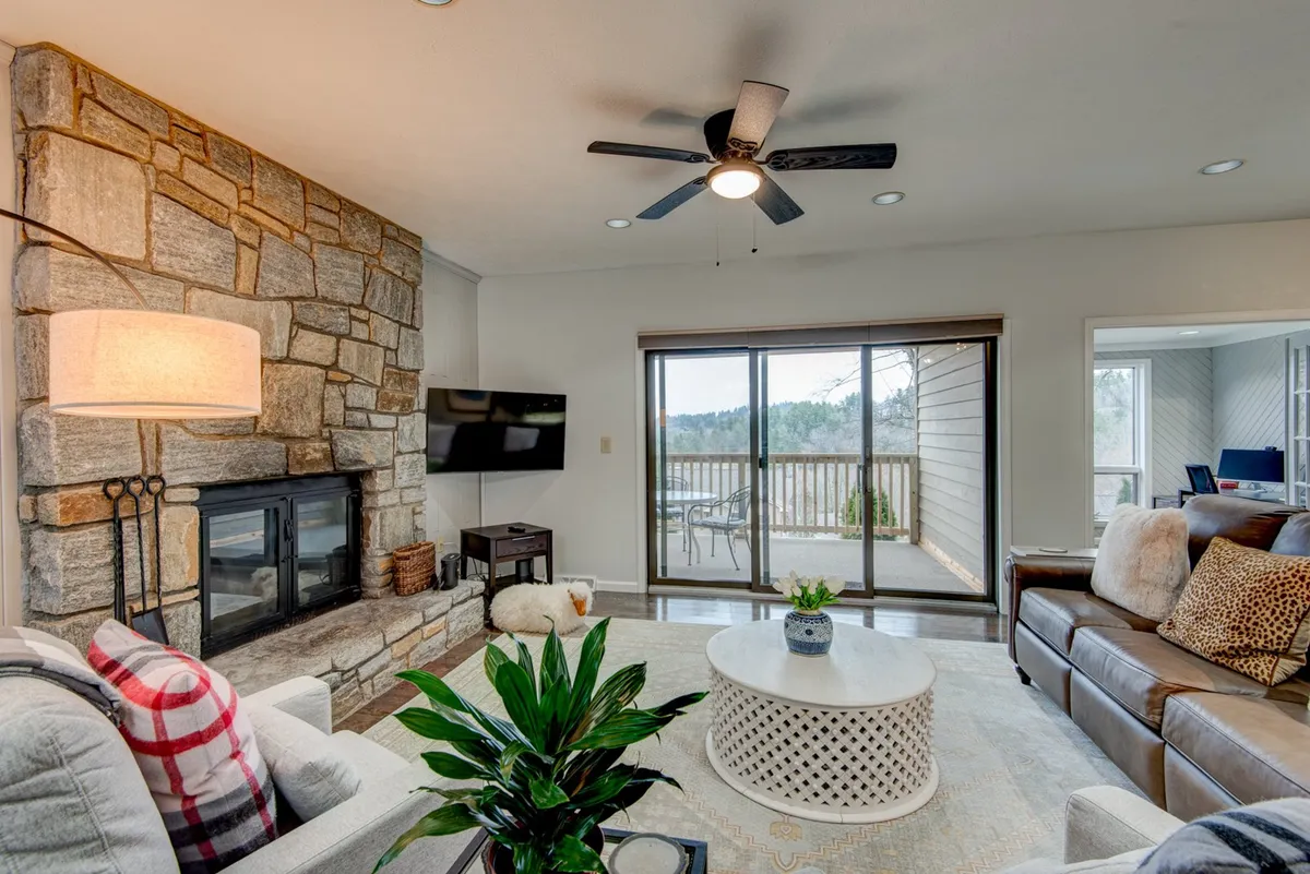A sun-drenched living room featuring a striking stone gas log fireplace, large windows that let in abundant natural light, and comfortable seating arranged for conversation and relaxation. The room’s inviting atmosphere is perfect for unwinding with family or entertaining guests.