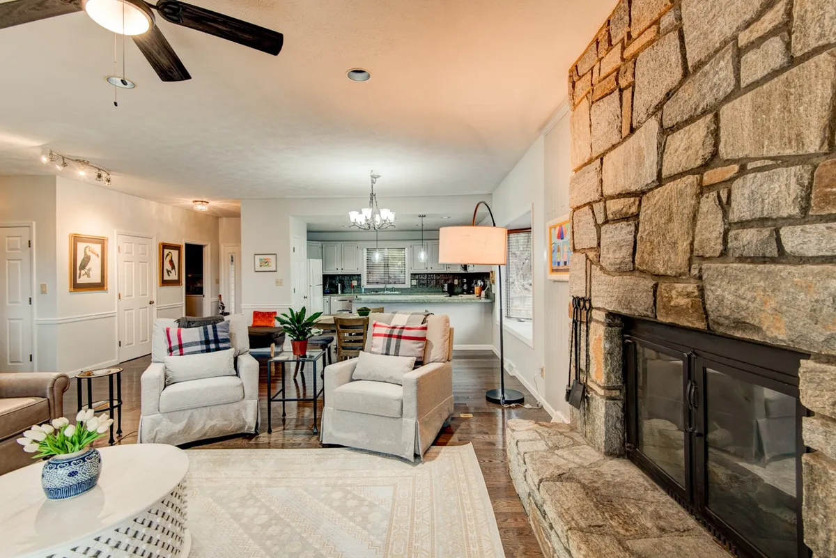 A cozy interior with a stone fireplace, comfortable armchairs, a decorative lamp, and a coffee table with a floral arrangement. The setting is intimate and perfect for relaxing or socializing after a day spent out in town.